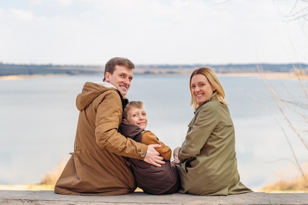 Young happy family sitting with beautiful lake view. parents with little boy kid