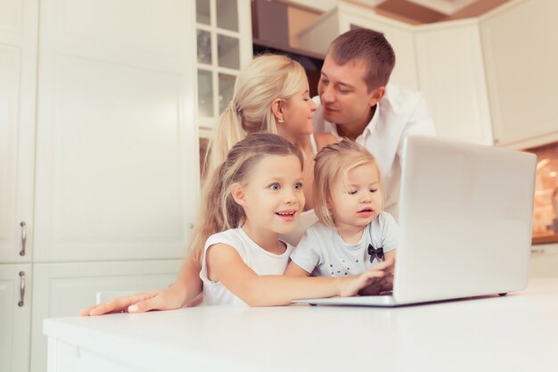 Молодая счастливая семья с помощью ноутбука, сидя на кухне дома