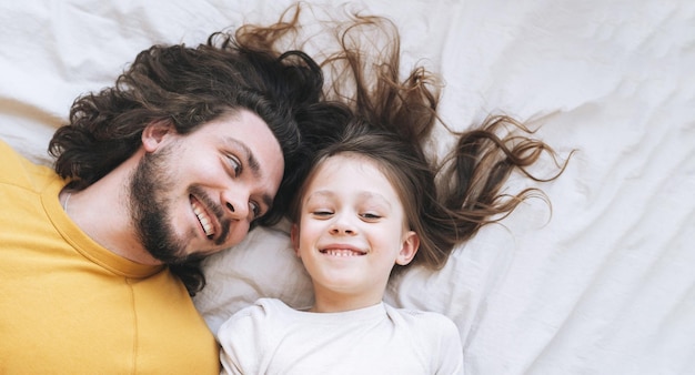 Giovane famiglia felice con padre e figlia barbuti sul letto in un'accogliente vista della casa dall'alto