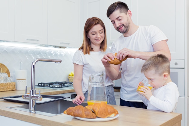 Young happy family with two young sons preparing breakfast together in their kitchen