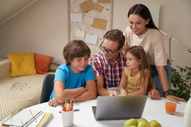 Фото Молодая счастливая семья, работающая на ноутбуке вместе с родителями, помогает детям с домашним заданием или учебой