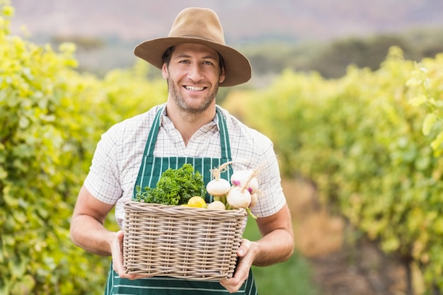 Young happy farmer holding a basket of vegetables