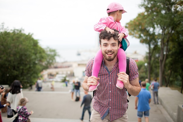 Young happy father hold child girl on his shoulders and pose on camera