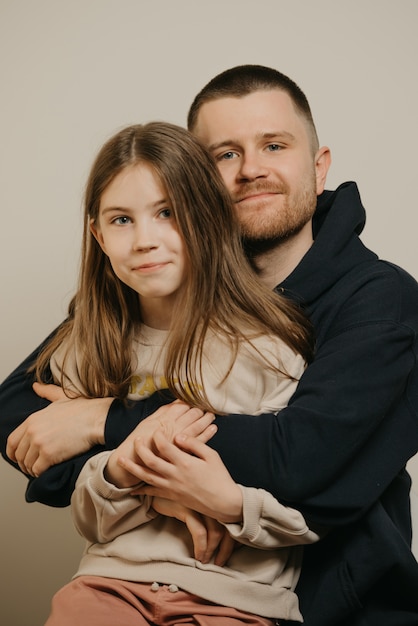 A young happy father with a beard hugs strongly his cute daughter.