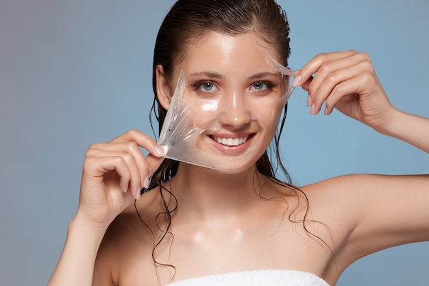 Young and happy female peeling off facial mask and smiling to the camera