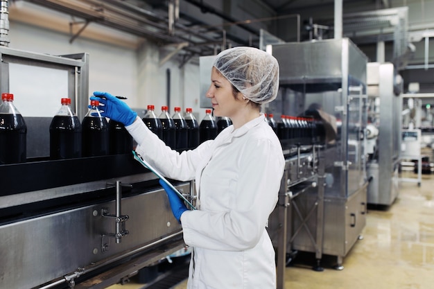 Young happy female worker in bottling factory checking juice bottles before shipment