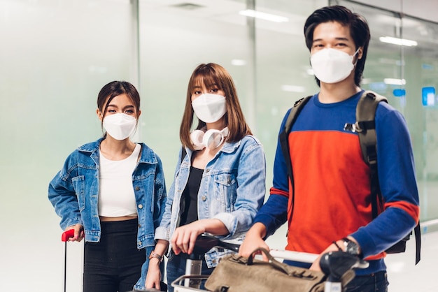 Un giovane amico viaggiatore felice in quarantena per coronavirus che indossa una maschera chirurgica per la protezione del viso tiene il passaporto e il biglietto prima del volo di una lunga vacanza al terminal internazionale dell'aeroporto