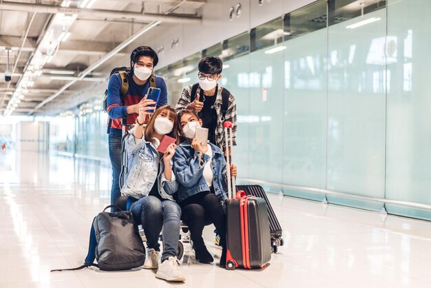 Young happy friend traveler in quarantine for coronavirus wearing surgical mask face protection look at camera making live selfie on smartphone before long travel vacation flight at airport