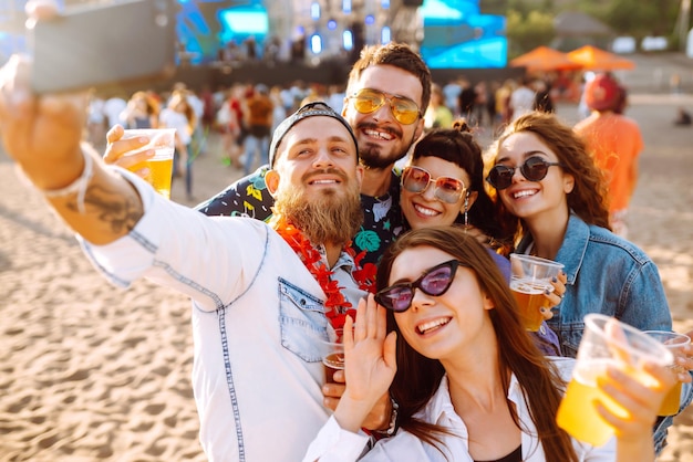Молодые счастливые друзья пьют пиво и веселятся на музыкальном фестивале вместе