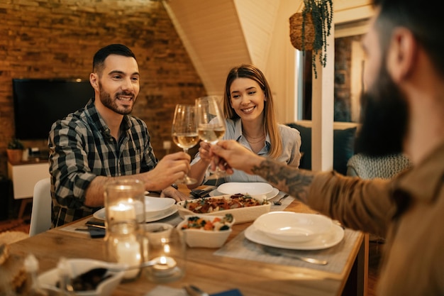 Young happy friends toasting with wine during dinner in dining room