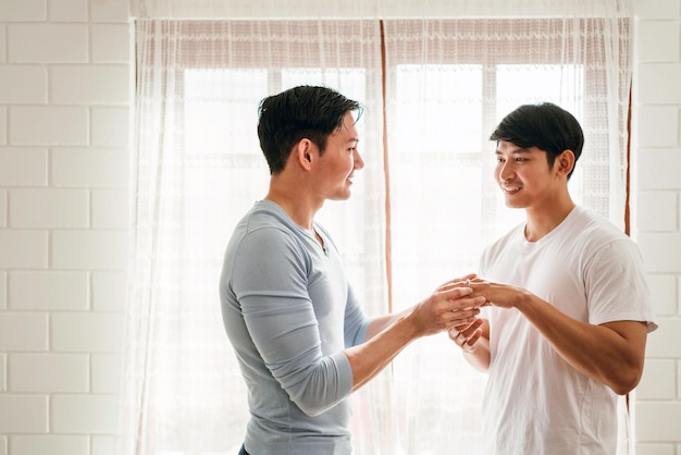 사랑에 빠진 젊은 행복한 게이 커플과 결혼 서프라이즈는 집 거실에서 결혼 반지를 끼고 있습니다. 게이 남성 제안 약혼 개념 놀란 파트너는 매우 행복합니다. 관계 목표