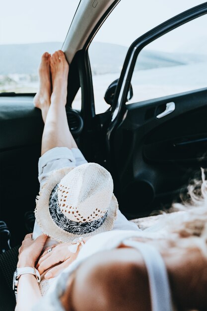 晴れた夏の日のビーチの海辺でドアを開けて車の中で休む若い幸せな女の子。旅行と休暇のコンセプト。