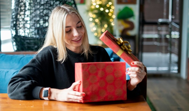 Una giovane ragazza felice apre la confezione regalo rossa