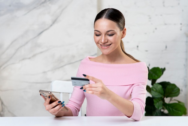 Giovane ragazza felice, donna positiva guardando la carta di credito che paga in linea in negozio, entra