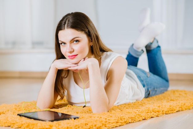 Young happy girl student lying on the floor and listening music from tablet indoors at home