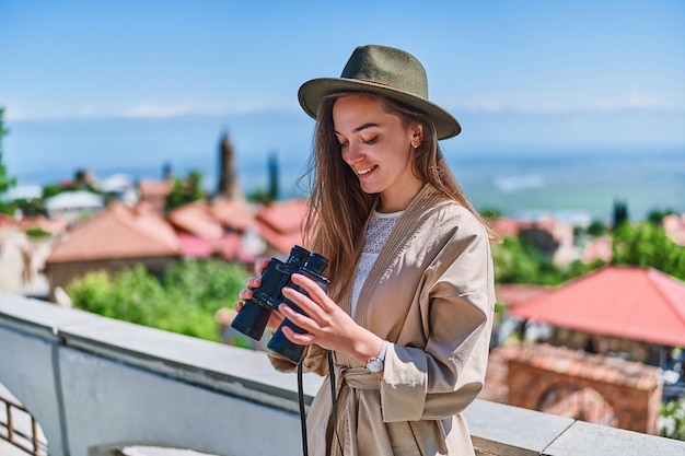 Young happy girl traveler wearing hat with binoculars during vacation weekend trip on a bright sunny day