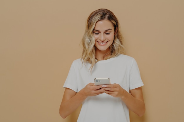 Young happy girl using smartphone chatting with boyfriend in social media and smiling