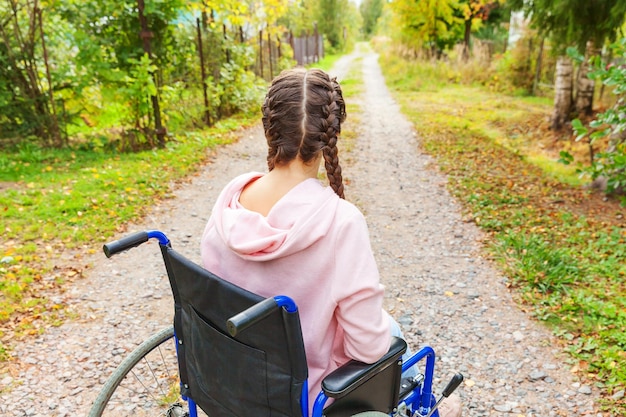 写真 病院の公園の道路で車椅子に乗った幸せな若い障害者女性が自由を楽しんでいます