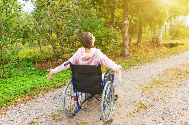 Young happy handicap woman in wheelchair on road in hospital park enjoying freedom