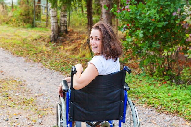 Young happy handicap woman in wheelchair on road in hospital park waiting for patient services