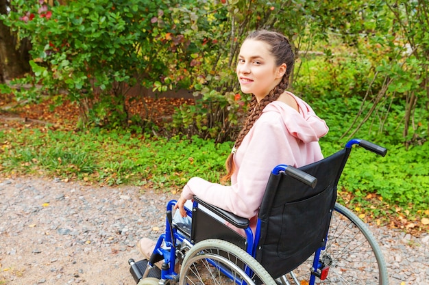 Young happy handicap woman in wheelchair on road in hospital park