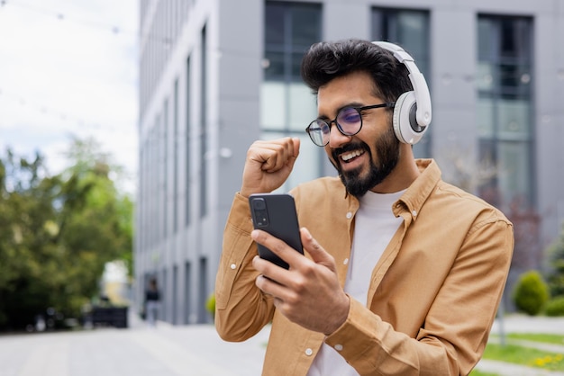 Young happy hindu man dancing on the street wearing headphones man using online application to