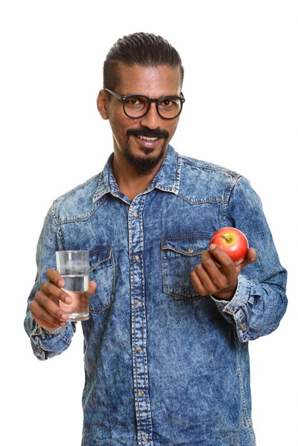 Young happy Indian man holding red apple and glass of water isolated