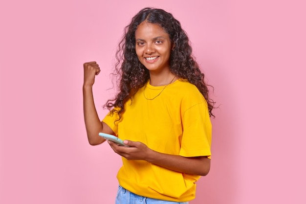 Young happy Indian woman with long hair makes victorious gesture and uses phone