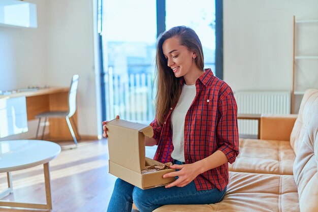 Young happy joyful smiling girl customer received parcel and unpacking cardboard box with online store order, good shipping delivery service