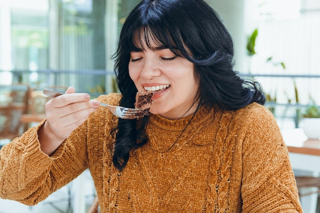 Young happy latin woman eating slice of chocolate cake