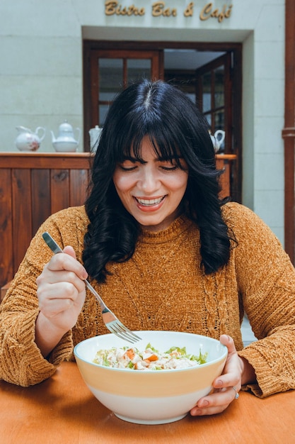 young happy latin woman sitting in restaurant watching bowl of delicious salad she is going to eat