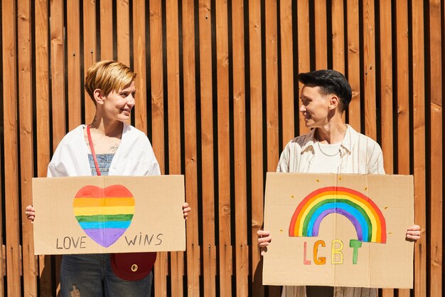 야외에서 서있는 동안 서로를보고 LGBT 징후와 플래 카드를 들고 젊은 행복 레즈비언