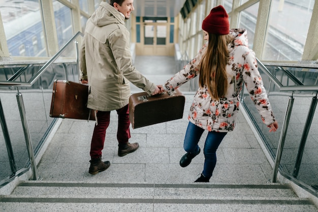 Young happy lovers carry vintage brown suitcases at railway station