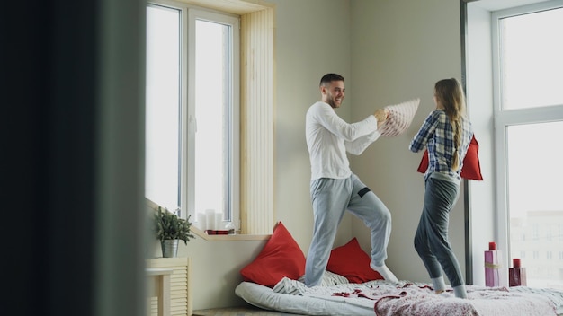 젊고 행복하고 사랑하는 부부는 아침에 집에서 침대에서 베개를 싸운다