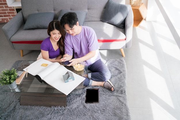 Young happy loving couple talking and using tablet to calculate the price of buying a house with a small wooden house model on a house drawing New home concept