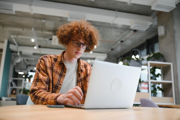 Photo young happy male freelancer in casual clothes sitting in cafe with laptop and using mobile phone