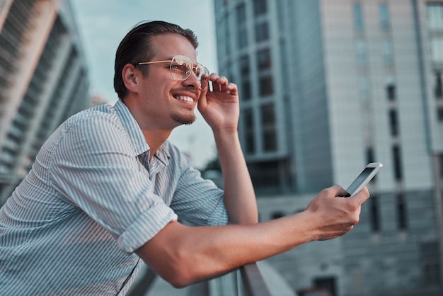 手に携帯電話を持って目をそらしている若い幸せな男。