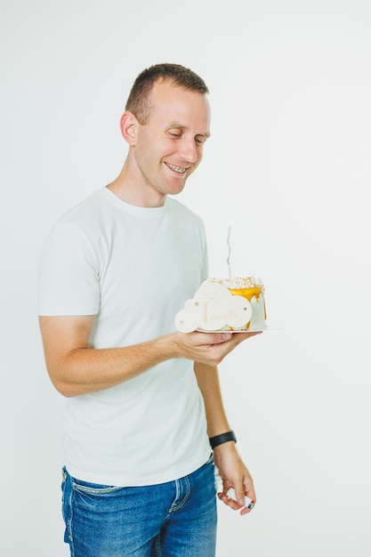 A young happy man holds a sweet cake in his hands while standing on a white background