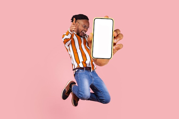 Young happy man jumping and showing his mobile phone display