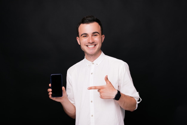 Young happy man pointing at his smartphone's screen on black background.