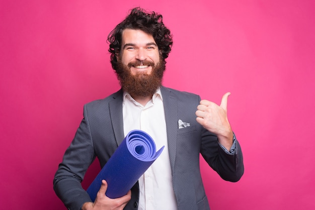 Young happy man showing a thumb up and holding a yoga mat