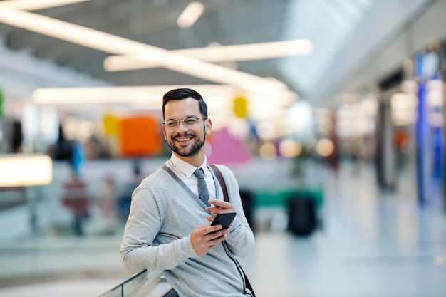 A young happy man in smart casual is standing at shopping mall with his phone