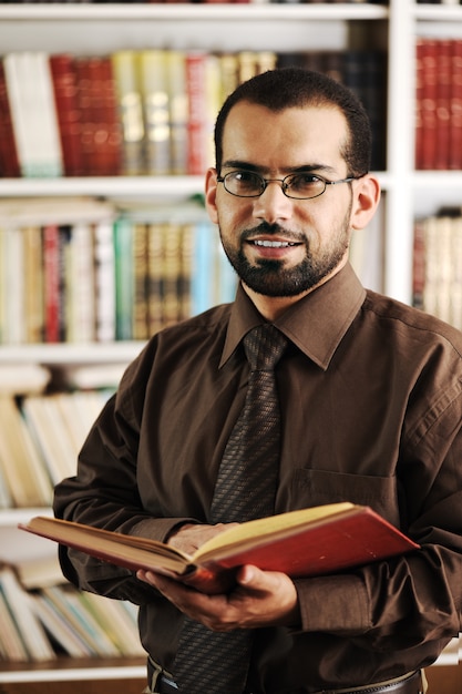 Young happy man standing in university library reading and smiling