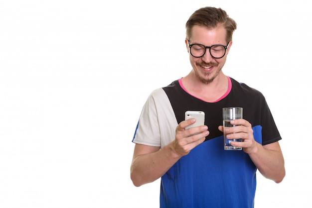 Young happy man using mobile phone and holding glass of water