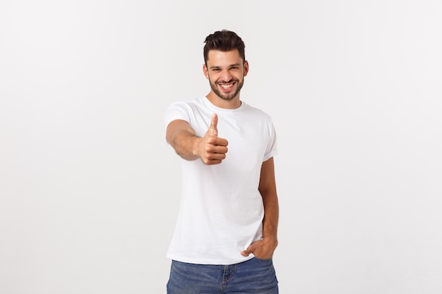 Young happy man with thumbs up sign in casuals isolated on white wall