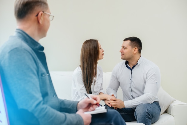 A young happy married couple of men and women talk to a\
psychologist at a therapy session. psychology.