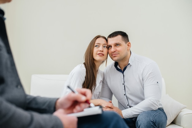 A young happy married couple of men and women talk to a\
psychologist at a therapy session. psychology.