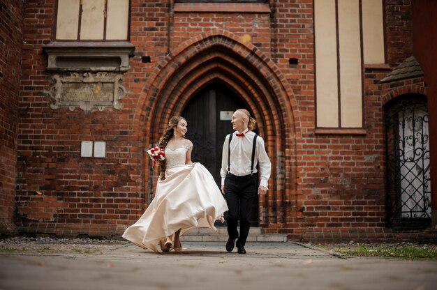 Young and happy married couple walking in a yard of old vintage red brick building with arch