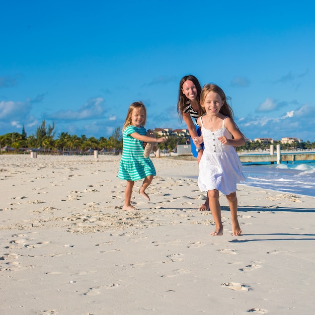 Young happy mother and her adorable daughters having fun at exotic beach on sunny day