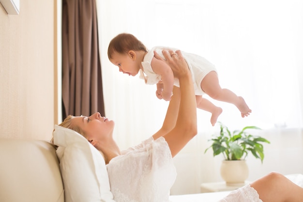 Young happy mother holding her baby in the bedroom